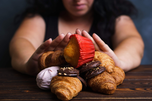 Person's hands holding assorted pastries and baked goods including croissants and chocolate cake over wooden surface