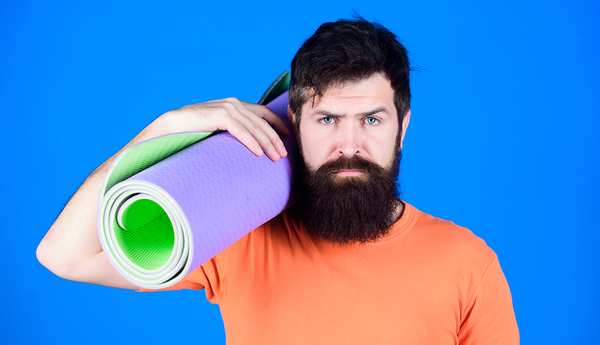 Bearded man in orange shirt holding rolled purple yoga mat with green interior against blue background