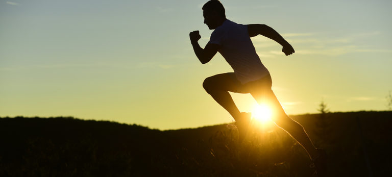 Silhouette of athlete running at sunset with backlit motion
