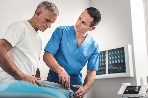 Chiropractor in blue scrubs examining patient's back in medical office