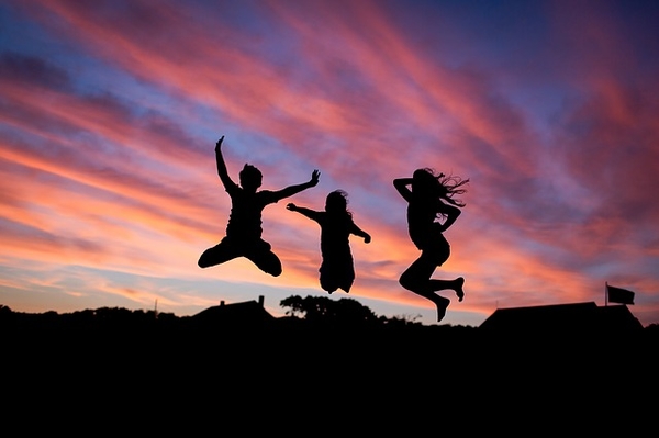 Three children silhouetted jumping against a dramatic sunset sky with orange and purple clouds