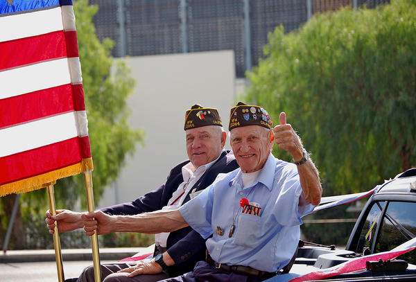 Two military veterans in dress uniforms holding an American flag during a parade or public event