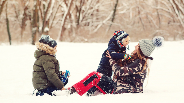 Two children and an adult sitting in snow wearing winter clothing and hats