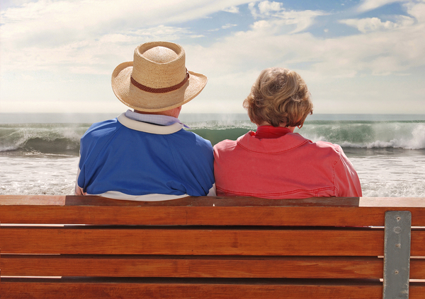Two people sitting on a wooden bench facing the ocean and beach