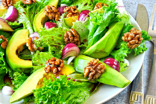 Green salad with avocado slices, walnuts, red onion, and mixed greens on white plate