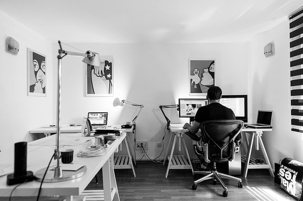 Black and white office space with two desks, computers, monitors, desk lamps, and a person seated at a workstation