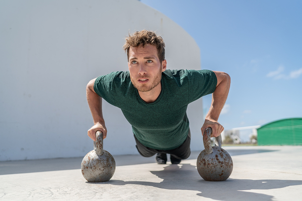 Man performing push-up exercise with kettlebells on outdoor concrete surface