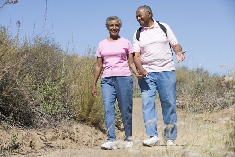 Senior couple walking together on a sandy trail with desert brush and clear blue sky