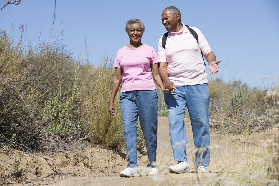 Senior couple walking together on a sandy trail with desert brush and clear blue sky