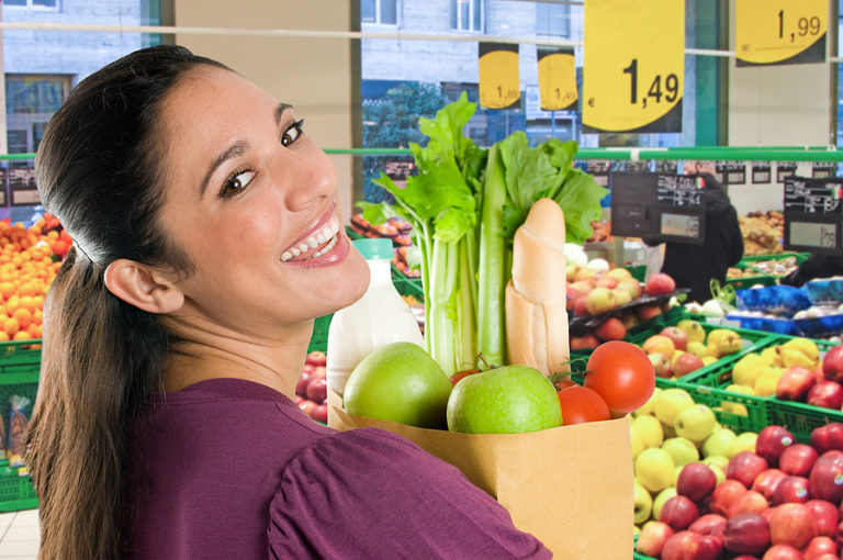 Woman holding paper grocery bag with fresh vegetables and fruit in grocery store produce section