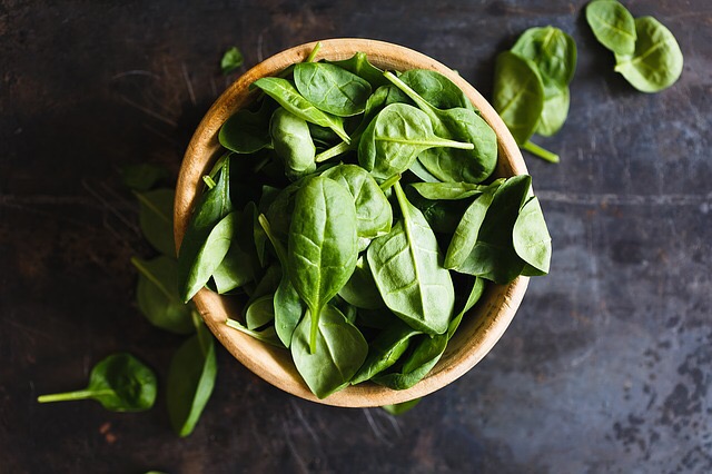 Fresh spinach leaves in a wooden bowl on a dark surface