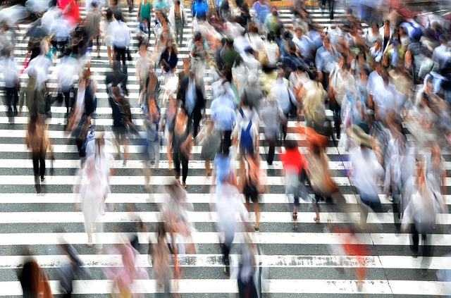Blurred overhead view of many pedestrians crossing a striped crosswalk in multiple directions