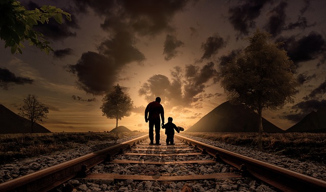 Adult and child silhouettes walking together on railroad tracks toward sunset between mountains