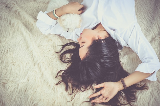 Person with long dark hair lying on fluffy white surface wearing white clothing and bracelets