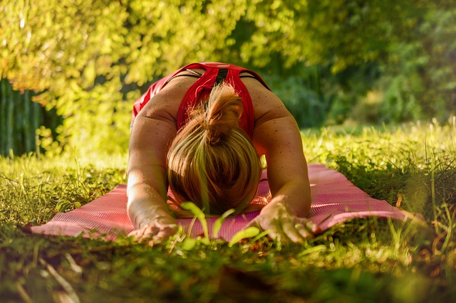 Person in red performing forward bend yoga pose on mat in outdoor garden setting