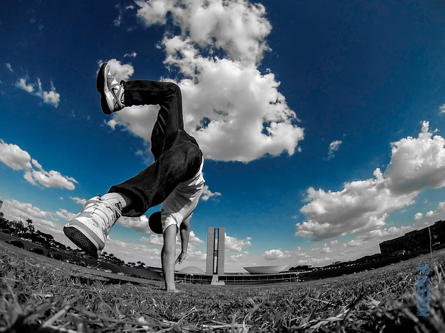 Person performing a backflip outdoors on grass with blue sky and clouds in background