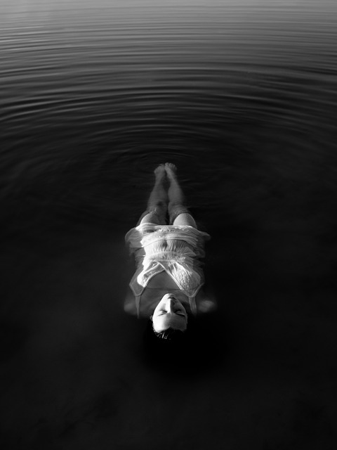 Person floating face-up in still water with concentric ripples radiating outward in black and white