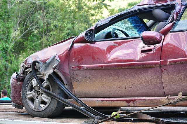 Red car with severe front-end damage from collision, showing crumpled hood and fender against green foliage background