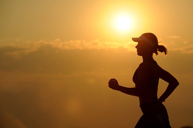 Silhouette of female runner jogging at sunset with golden sky background