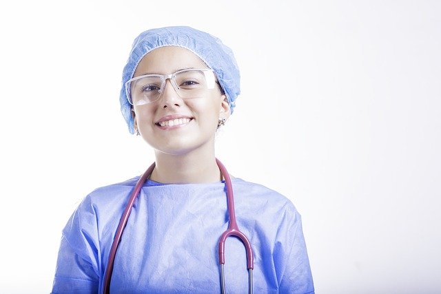 Smiling healthcare professional wearing blue surgical cap, glasses, and stethoscope