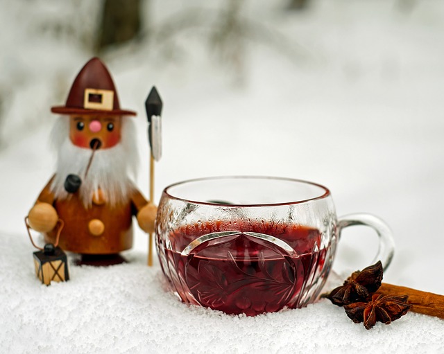Glass mug of dark red tea with cinnamon stick and star anise on snow next to decorative gnome figurine