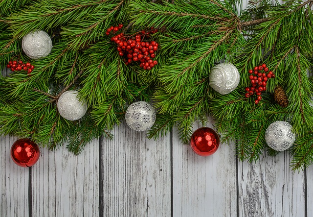 Evergreen branches with red and silver ornaments and red berries on whitewashed wood surface