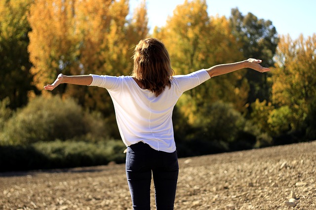 Woman with arms outstretched in open field with autumn trees in background