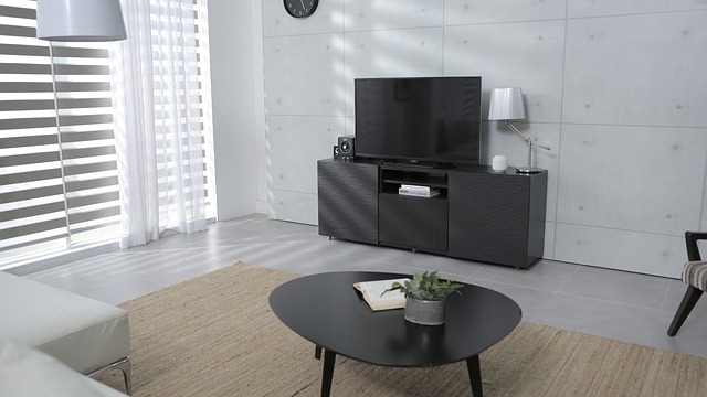 Modern living room with black TV stand, flat-screen television, round black coffee table, and white furniture near striped window blinds