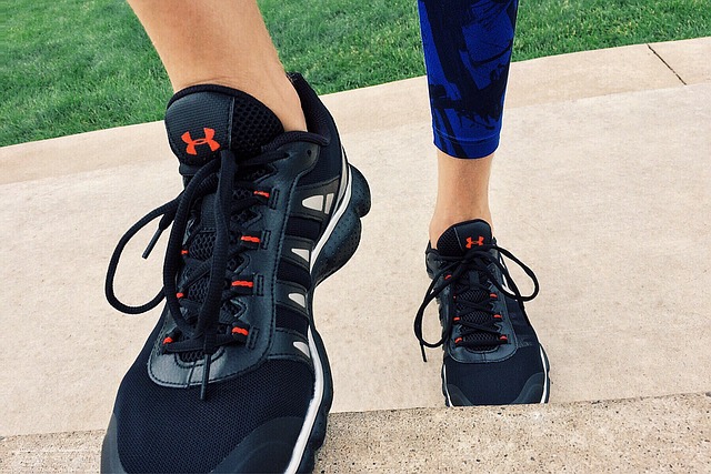 Person wearing black athletic shoes with orange accents standing on concrete beside grass