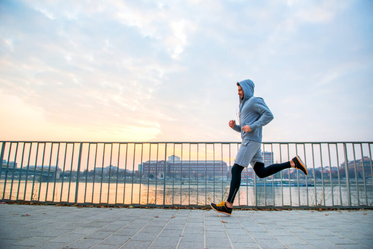 Runner jogging on waterfront path with city skyline and railing in background