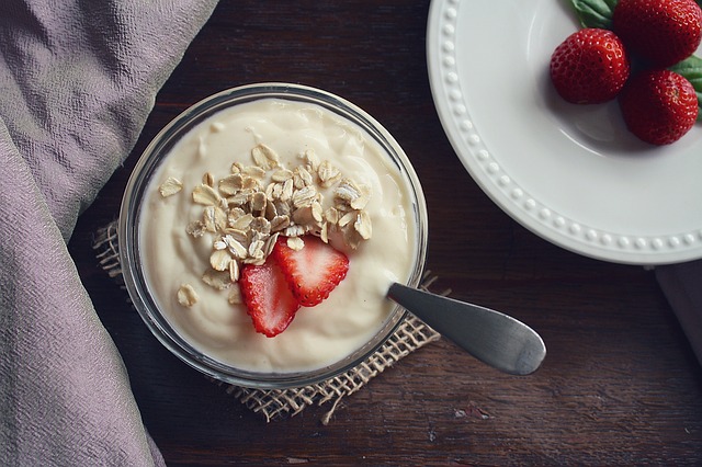 Bowl of yogurt topped with sliced strawberries and granola, served with fresh strawberries on a white plate