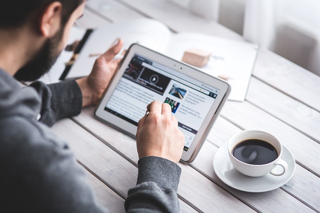 Man using tablet at white desk with coffee cup and papers nearby