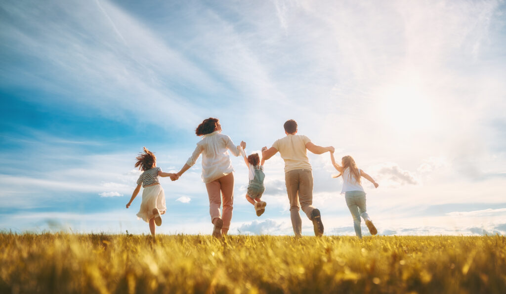 Family holding hands running together through an open field under blue sky
