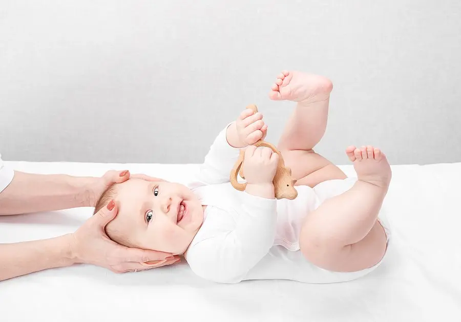 A smiling baby lying on her back while a practitioner's hands gently cradle her head