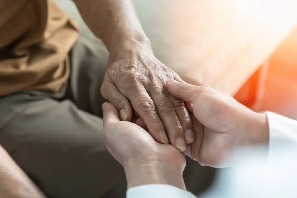 Two hands gently holding an older person's hand