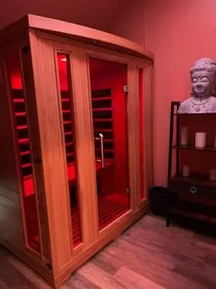 A cedar infrared sauna glowing red inside, beside a shelf with candles and a stone Buddha